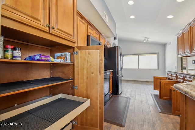 kitchen with lofted ceiling, light wood-type flooring, brown cabinets, range, and freestanding refrigerator