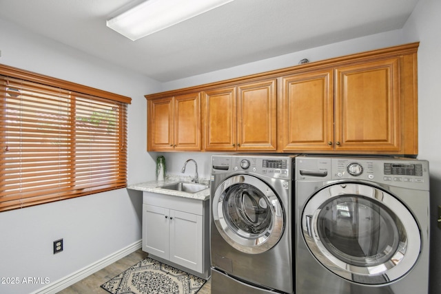 clothes washing area with cabinet space, a sink, separate washer and dryer, light wood-type flooring, and baseboards