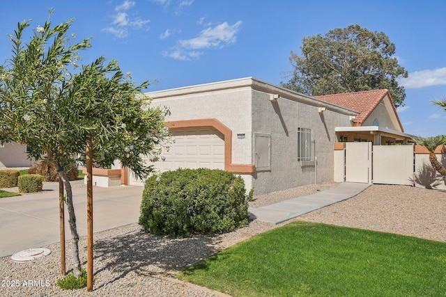 view of side of home with stucco siding, an attached garage, a gate, driveway, and a tiled roof