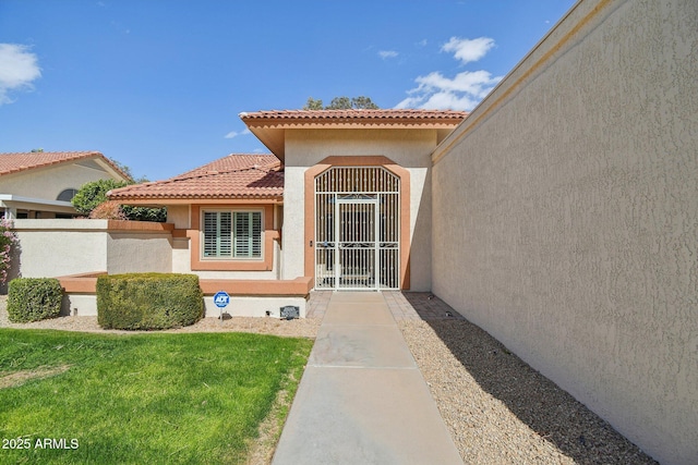 doorway to property featuring a tiled roof, fence, a lawn, and stucco siding