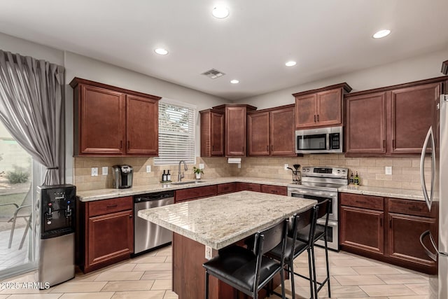 kitchen with light stone counters, stainless steel appliances, a kitchen island, a kitchen breakfast bar, and sink