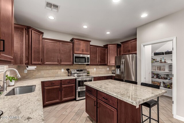 kitchen with appliances with stainless steel finishes, a breakfast bar, light stone countertops, and sink