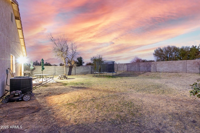 view of yard featuring a trampoline, an outdoor fire pit, a fenced backyard, and cooling unit