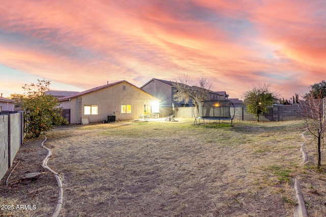 back of property with a trampoline, a fenced backyard, and a lawn