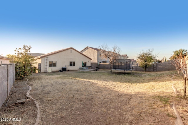 rear view of property with a trampoline, a fenced backyard, a patio, and stucco siding