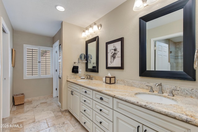 bathroom featuring double vanity, a sink, stone tile flooring, and baseboards