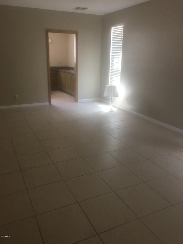 empty room with light tile patterned floors, visible vents, and baseboards