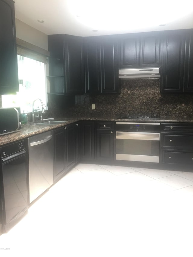 kitchen featuring under cabinet range hood, dark cabinetry, stainless steel dishwasher, and oven