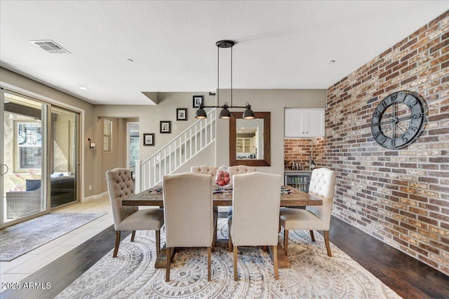 dining room featuring stairway, wood finished floors, brick wall, baseboards, and visible vents