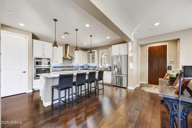 kitchen with wall chimney range hood, dark wood-style flooring, tasteful backsplash, and appliances with stainless steel finishes
