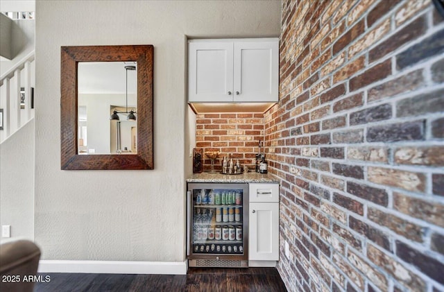 bar featuring baseboards, dark wood finished floors, brick wall, beverage cooler, and a bar
