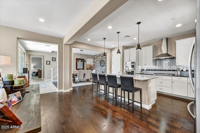 kitchen featuring appliances with stainless steel finishes, decorative backsplash, dark wood-style floors, and wall chimney exhaust hood