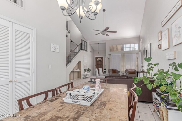 dining space with light tile patterned flooring, high vaulted ceiling, ceiling fan with notable chandelier, stairs, and visible vents
