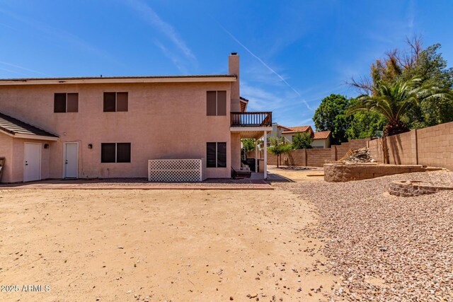 back of house with fence, a balcony, a patio, stucco siding, and a chimney