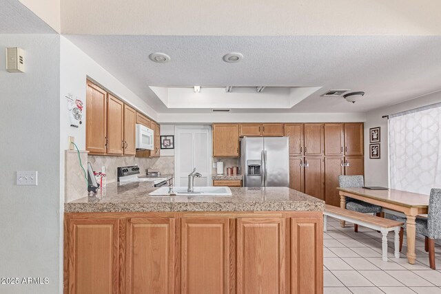 kitchen with a sink, a raised ceiling, white appliances, a textured ceiling, and a peninsula