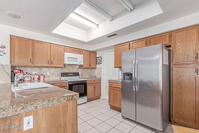kitchen featuring visible vents, electric range, white microwave, stainless steel fridge, and a sink
