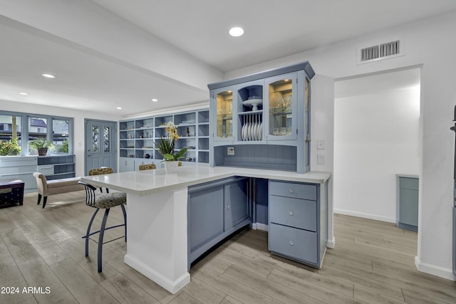 kitchen featuring kitchen peninsula, light hardwood / wood-style floors, light stone counters, and a breakfast bar area