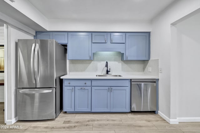 kitchen with sink, stainless steel appliances, tasteful backsplash, blue cabinets, and light wood-type flooring