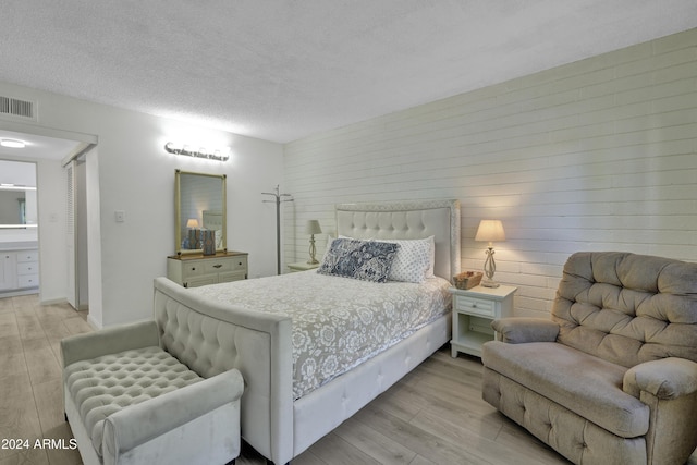 bedroom featuring ensuite bath, a textured ceiling, and light hardwood / wood-style flooring