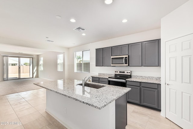 kitchen featuring sink, gray cabinetry, light stone counters, stainless steel appliances, and a kitchen island with sink