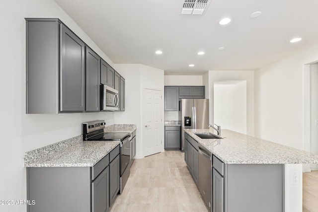 kitchen with appliances with stainless steel finishes, sink, gray cabinetry, light stone counters, and a center island with sink