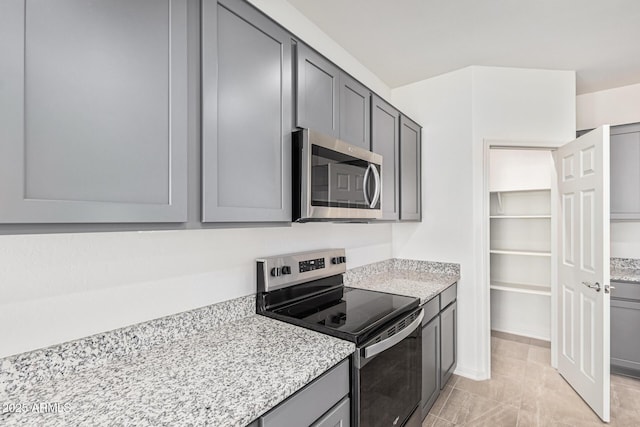 kitchen with light stone countertops, gray cabinets, and stainless steel appliances