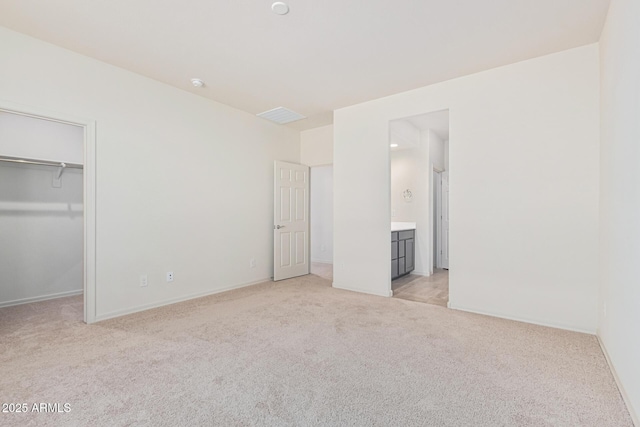 unfurnished bedroom featuring ensuite bathroom, a walk in closet, light carpet, and a closet