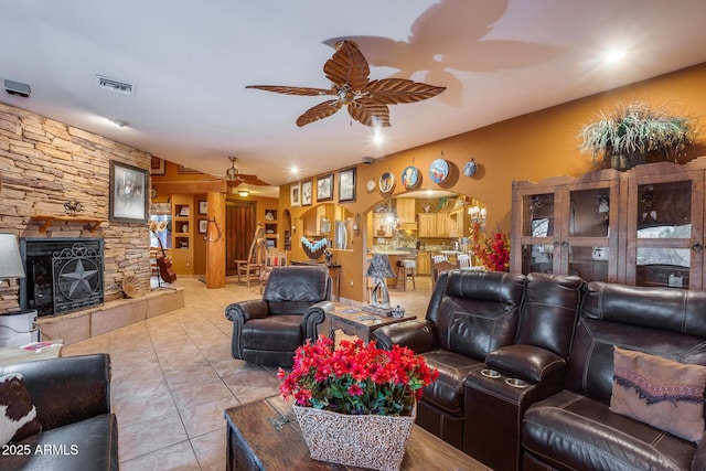 tiled living room with a stone fireplace and ceiling fan