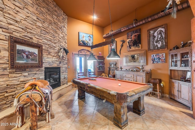 game room featuring light tile patterned floors, a towering ceiling, a stone fireplace, and pool table