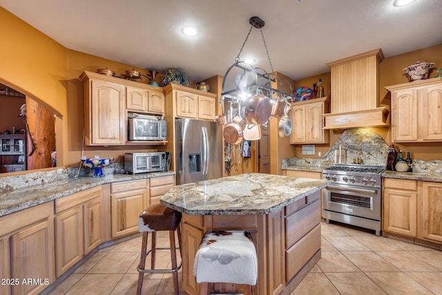 kitchen featuring light stone countertops, stainless steel appliances, light brown cabinetry, and a kitchen island