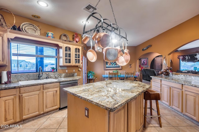 kitchen featuring light brown cabinetry, sink, a center island, stainless steel dishwasher, and light stone counters