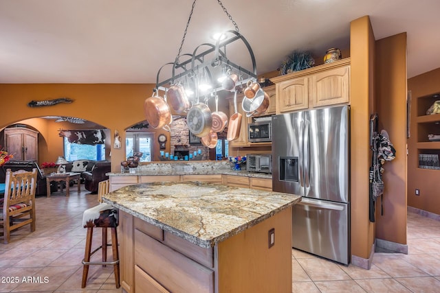 kitchen with light tile patterned floors, light stone countertops, a center island, and appliances with stainless steel finishes