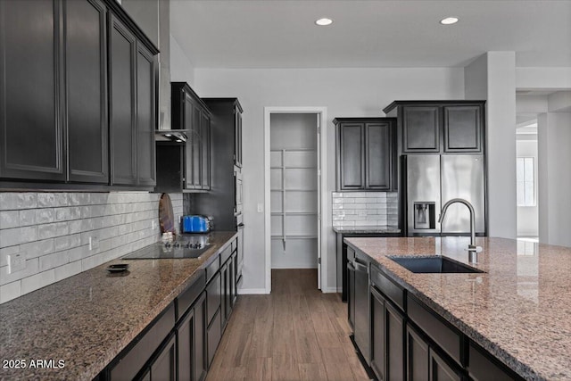 kitchen featuring wood finished floors, stainless steel fridge with ice dispenser, stone countertops, a sink, and black electric cooktop