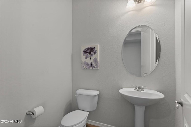 bathroom featuring toilet, baseboards, and a sink