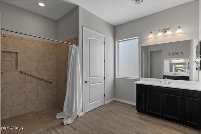 full bath with vanity, wood finished floors, baseboards, and a tile shower