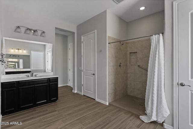 bathroom featuring tiled shower, vanity, baseboards, and wood finished floors