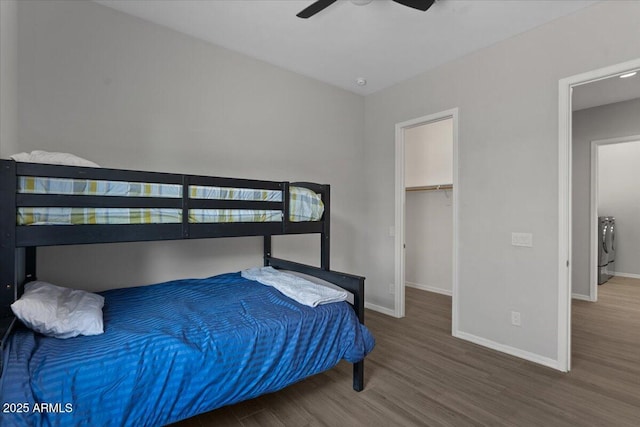 bedroom with a spacious closet, ceiling fan, baseboards, washing machine and dryer, and wood finished floors