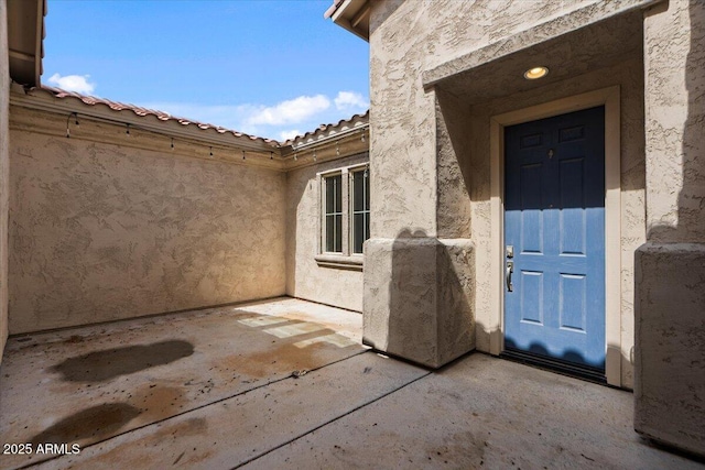 entrance to property with stucco siding, a patio, and a tiled roof