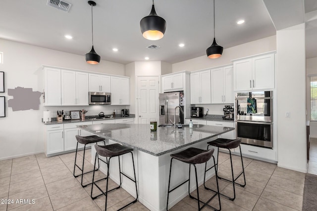 kitchen featuring appliances with stainless steel finishes, a kitchen island with sink, sink, stone counters, and white cabinets