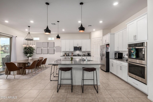 kitchen featuring dark stone counters, sink, an island with sink, and stainless steel appliances