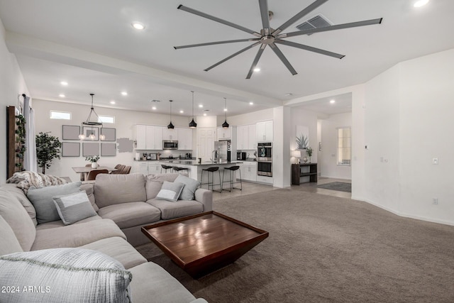 living room featuring beamed ceiling, carpet, and ceiling fan with notable chandelier