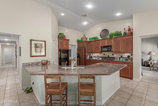 kitchen featuring light tile patterned flooring, sink, kitchen peninsula, black appliances, and a kitchen breakfast bar