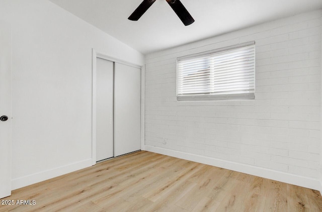 unfurnished bedroom featuring brick wall, vaulted ceiling, ceiling fan, hardwood / wood-style floors, and a closet