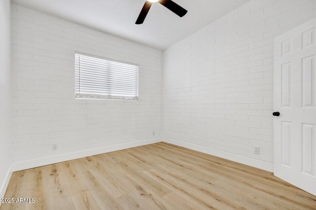 empty room with light hardwood / wood-style flooring, ceiling fan, and brick wall