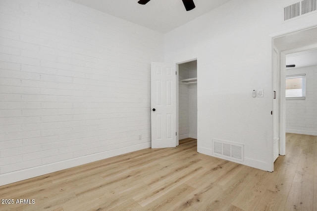 unfurnished bedroom featuring ceiling fan, a closet, brick wall, and light wood-type flooring