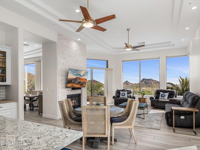 13621 E Aster Dr, Scottsdale, AZ 85259 - dining space featuring a stone fireplace, a tray ceiling, a healthy amount of sunlight, and ceiling fan