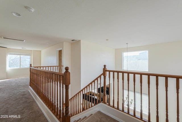 corridor with carpet floors, visible vents, and an upstairs landing