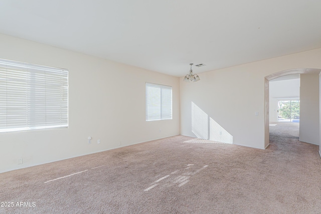 empty room with arched walkways, visible vents, light carpet, and an inviting chandelier