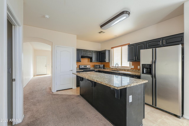 kitchen featuring visible vents, light colored carpet, a center island, stainless steel appliances, and a sink