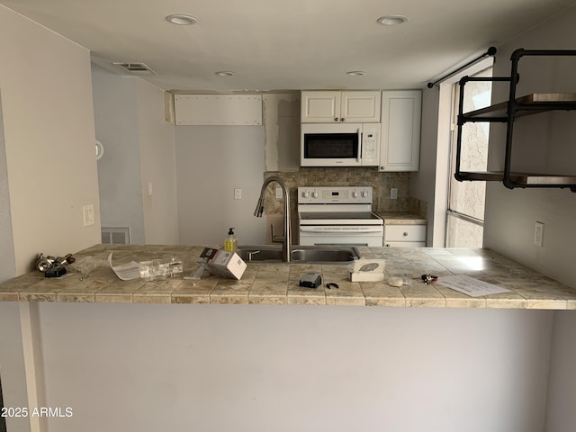 kitchen with sink, white appliances, white cabinetry, tasteful backsplash, and kitchen peninsula